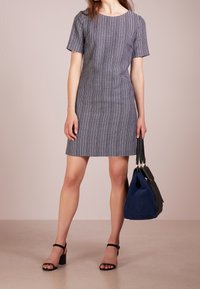 Šaty krátkého rukávu v námořnické modré a bílé geometrické vzoru, doplněné černou a modrou taškou. Mají přiléhavý střih a kulatý výstřih.