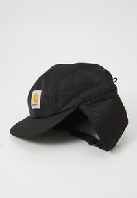 Cappello isolato nero con visiera curva, dotato di orecchino foderato in pile e un logo Carhartt bianco e giallo sul davanti.