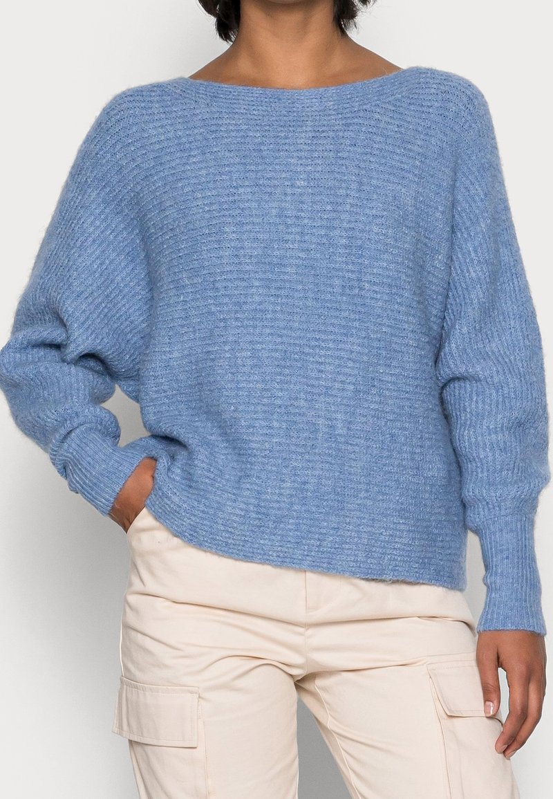 Pull bleu clair tricoté avec un large col, épaules tombantes et poignets côtelés. Présente une finition douce et texturée ainsi qu'une coupe décontractée.