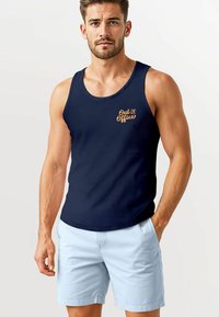 Navy tank top with "Out of Office" orange text, worn with light blue shorts. The fabric appears smooth with a classic fit design.