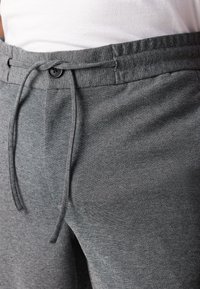 Pantaloni de trening gri cu talie ajustabilă, închidere cu buton și țesătură texturată, care pun accent pe confort și o croială lejeră.
