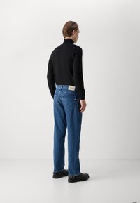 Camisa negra de manga larga, jeans de mezclilla azules con etiqueta trasera, diseño sencillo, corte recto, tejido resistente, combinados con zapatos negros.