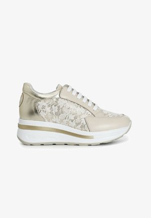 Sneaker beige con lacci, con un accento metallico dorato, sovrapposizione di pizzo testurizzato e suola bianca con una striscia dorata.