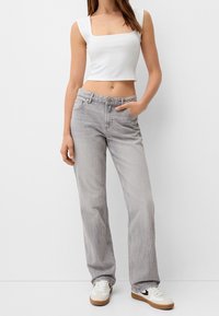 Top corto bianco e jeans dritti grigi chiari, con tasche, bottone e cuciture a contrasto. Completato con sneakers bianche.