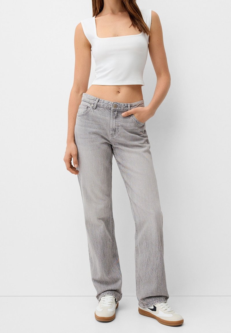 Top corto bianco e jeans dritti grigi chiari, con tasche, bottone e cuciture a contrasto. Completato con sneakers bianche.