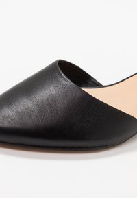 Chaussure en cuir noir à enfiler avec un bout pointu, texture lisse et intérieur nude. Caractéristiques d'un design minimaliste sans quincaillerie visible.