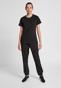 Sort bomuld t-shirt med korte ærmer, parret med sorte sweatpants med ribbede manchetter og en lille logo-detail. Sorte træningssko.