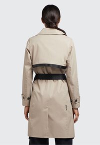 Beige trenchcoat med bälte i midjan. Har klassisk krage, långa ärmar, knappdetaljer och ett svart märkesbälte på baksidan.