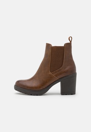 Brauner Leder-Stiefelette mit Blockabsatz, elastischem Seitenteil, Zuglasche hinten und schwarzer profillierter Sohle vor hellem Hintergrund.