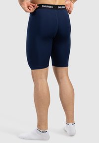 Pantaloni corti blu navy realizzati in materiale elastico, con una vita nera recante il logo "SMILODOX". La vista mostra il retro e le gambe.