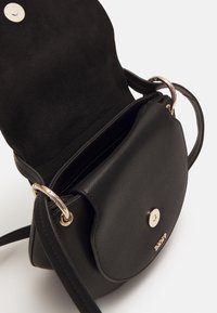 Borsa a tracolla in pelle nera con patta aperta, chiusura magnetica dorata e hardware circolare dorato sulla tracolla regolabile.