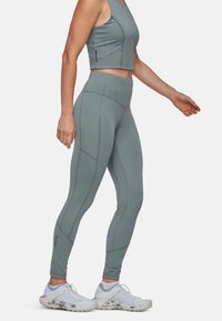 Ensemble de sport en deux pièces dans un vert discret, comprenant un débardeur court avec des détails de couture et un legging taille haute avec poches latérales.