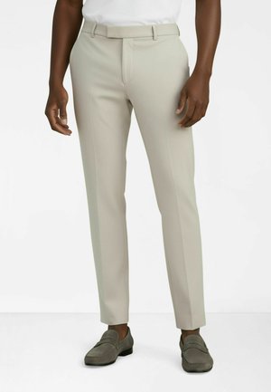 Jasnobeżowe, dopasowane spodnie z płaskim przodem, wąskim krojem i minimalistycznym designem. Połączone z szarymi butami wsuwanymi. Gładka tekstura.
