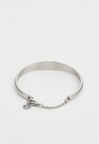 Bracciale a manichetta in metallo argentato con una finitura liscia, un'apertura a forma di cuore e una catena decorativa con un ciondolo circolare attaccato.