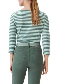 Grün gestreiftes langärmliges Hemd mit Rundhalsausschnitt, kombiniert mit hochgeschnittenen grünen Jeans mit Gesäßtaschen und Gürtelschlaufen.