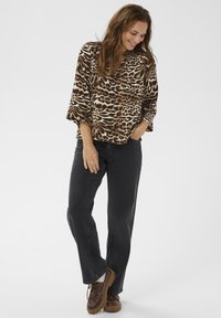 Blus med leopardtryck och 3/4-ärmar, i kombination med svarta raka jeans och bruna snörskor, som skapar en avslappnad look.