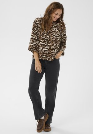 Bluza s uzorkom leoparda s rukavima do 3/4, u kombinaciji s crnim ravnim trapericama i smeškim cipelicama sa pertlama, stvarajući opušten izgled.