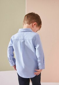 Camicia azzurro chiaro a maniche lunghe con colletto, polsini con bottoni e un tessuto texturizzato; vista dal retro.