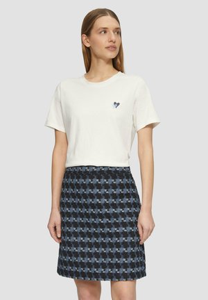 Witte katoenen t-shirt met een klein blauw hartgrafiek, gecombineerd met een rok van middelgrote lengte met een blauw en zwart houndstooth patroon, van textuurstof.