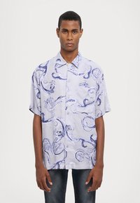 Camisa de manga corta de color lila claro con patrones en espiral azules, cuello puntiagudo y un bolsillo en el pecho, confeccionada en una tela suave.