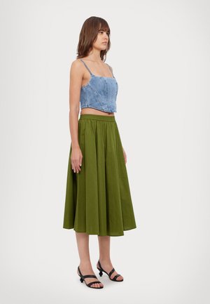 Top corto de mezclilla con tirantes finos, combinado con una falda larga y fluida verde. Sandalias negras con tiras completan el atuendo.