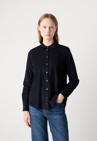 Chemise boutonnée bleu marine foncé avec col, manches longues et coupe décontractée. Présente des boutons blancs et une finition en tissu texturé subtile.