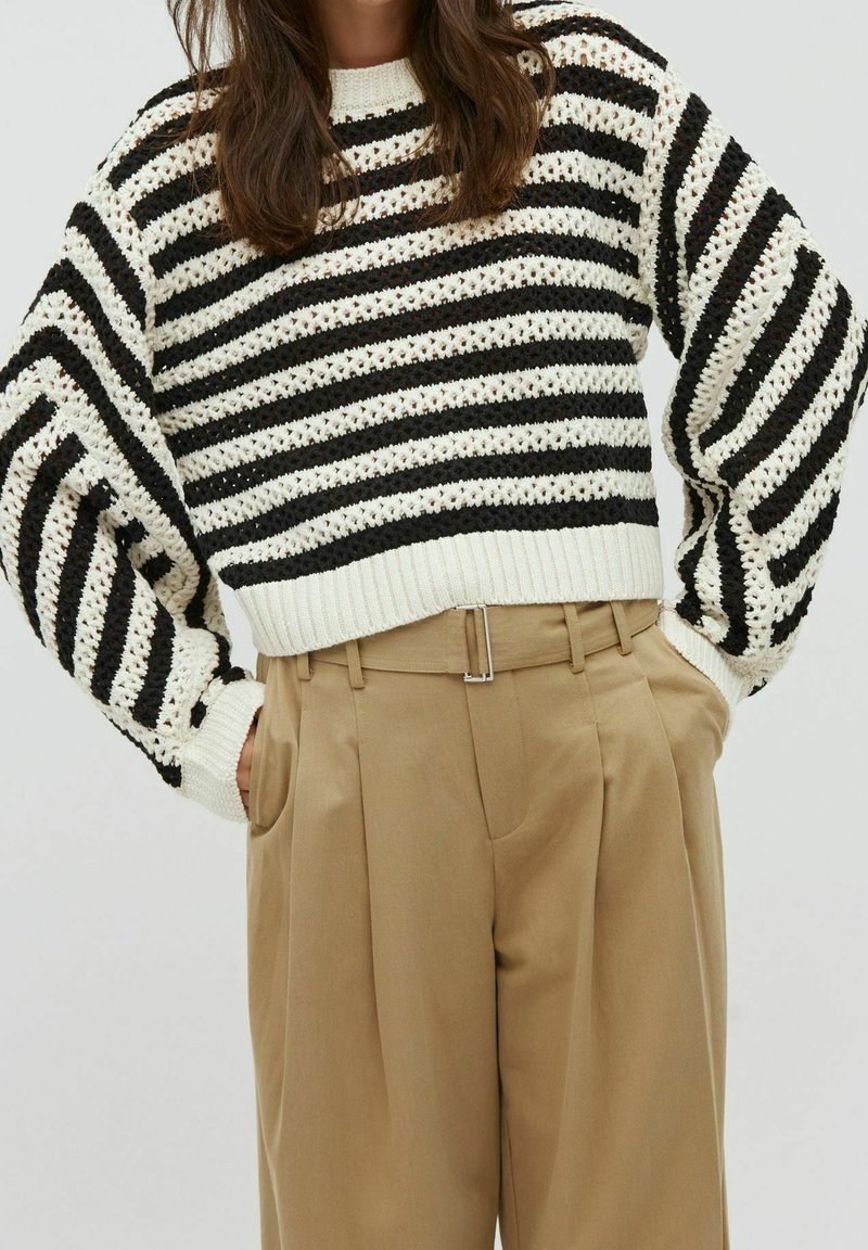 Černobílý pruhovaný pletený svetr s volnými rameny a žebrovaným límcem, kombinovaný s béžovými kalhotami s vysokým pasem a stříbrnou sponou.