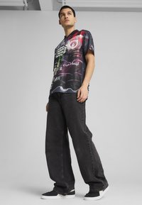 Camiseta gráfica multicolorida de corte relajado, con texto y diseños en varios colores, combinada con jeans de mezclilla gris oscuro sueltos y zapatillas.