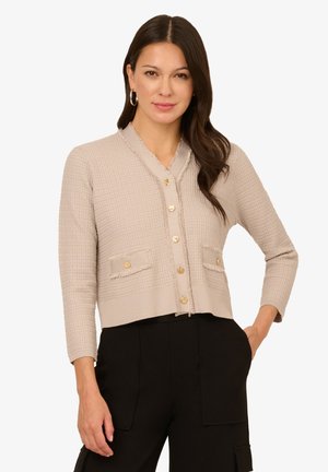 Beige verkürzter Cardigan aus strukturiertem Stoff mit langen Ärmeln und goldenen Knöpfen. Mit zwei vorderen Taschen und einem lockeren Schnitt.