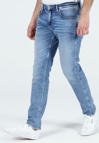 Jasnoniebieskie dżinsy o slim fit, z wyblakłym teksturem, klasycznym pięciopocketowym designem i białymi przeszyciami, w połączeniu z białymi sneakerami.