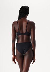 Conjunto de biquíni preto com um top de soutien com alças ajustáveis e fecho de clip, combinado com cuecas de biquíni de cintura baixa, ambos feitos de um tecido suave.