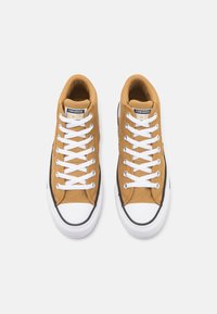 Hnědé plátěné vysoké tenisky s bílými šňůrkami, černými akcenty a bílou gumovou špičkou, které mají klasické logo Converse All Star.