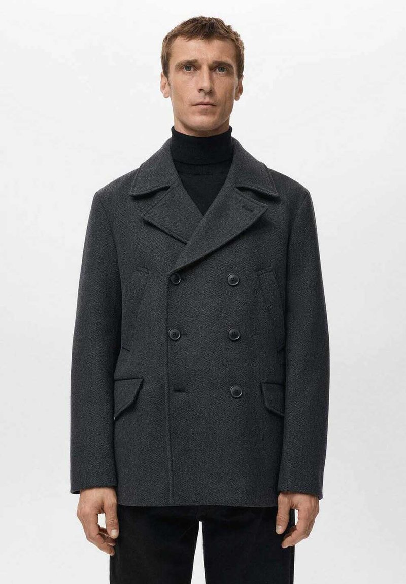 Abrigo gris cruzado de lana texturizada con solapas grandes, dos bolsillos delanteros y botones negros. Llevado sobre un jersey de cuello alto negro.