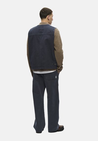 Costum din materiale mixte în nuanțe de bleumarin și maro, care include o vestă fără mâneci și pantaloni largi, având un design texturat și cu mâneci moi.