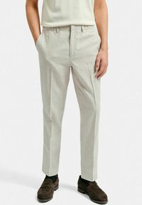 Ljust grå byxor med skräddarsydd passform, tillverkade av ett mjukt tyg. Har flat front, sidfickor och en veck ner längs benen.