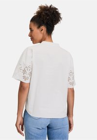 Blusa bianca con maniche corte a palloncino che presenta motivi floreali ricamati ai polsini. Tessuto di cotone, vestibilità comoda, scollatura rotonda.