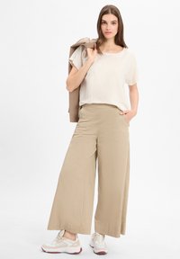 Beige wijde broek met zijzakken, gecombineerd met een losse lichte top, geaccentueerd met een beige blazer en witte sneakers.