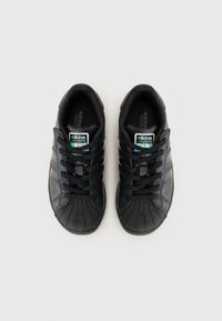 Μαύρα αθλητικά παπού�τσια Adidas με υφή στην άκρη, τρεις πλευρικές ρίγες, ίσια κορδόνια και ετικέτα πολύχρωμων LED φώτων στη γλώσσα.