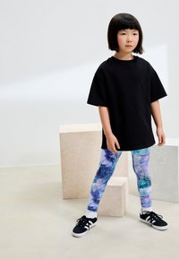 Svart oversized t-shirt, färgglada leggings med abstrakt mönster i blå och lila toner, och svarta sneakers med vita sulor.