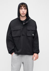 Μαύρο μπουφάν με κουκούλα, δύο μεγάλες τσέπες με καπάκι, κλείσιμο με φερμουάρ και ριμπ μανσέτες. Κατασκευασμένο από υφασμάτινη υφή, με μικρή λεπτομέρεια λογότυπου.