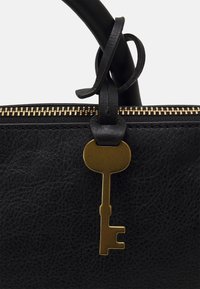 Czarna skórzana torba z uchwytem, do którego przymocowany jest złoty urok w stylu retro w kształcie klucza, blisko złotego suwaka.
