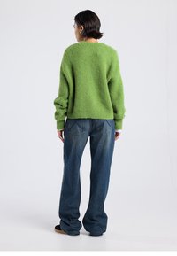Green knitted sweater with a loose fit, round neck, and long sleeves, paired with dark blue wide-leg denim jeans.