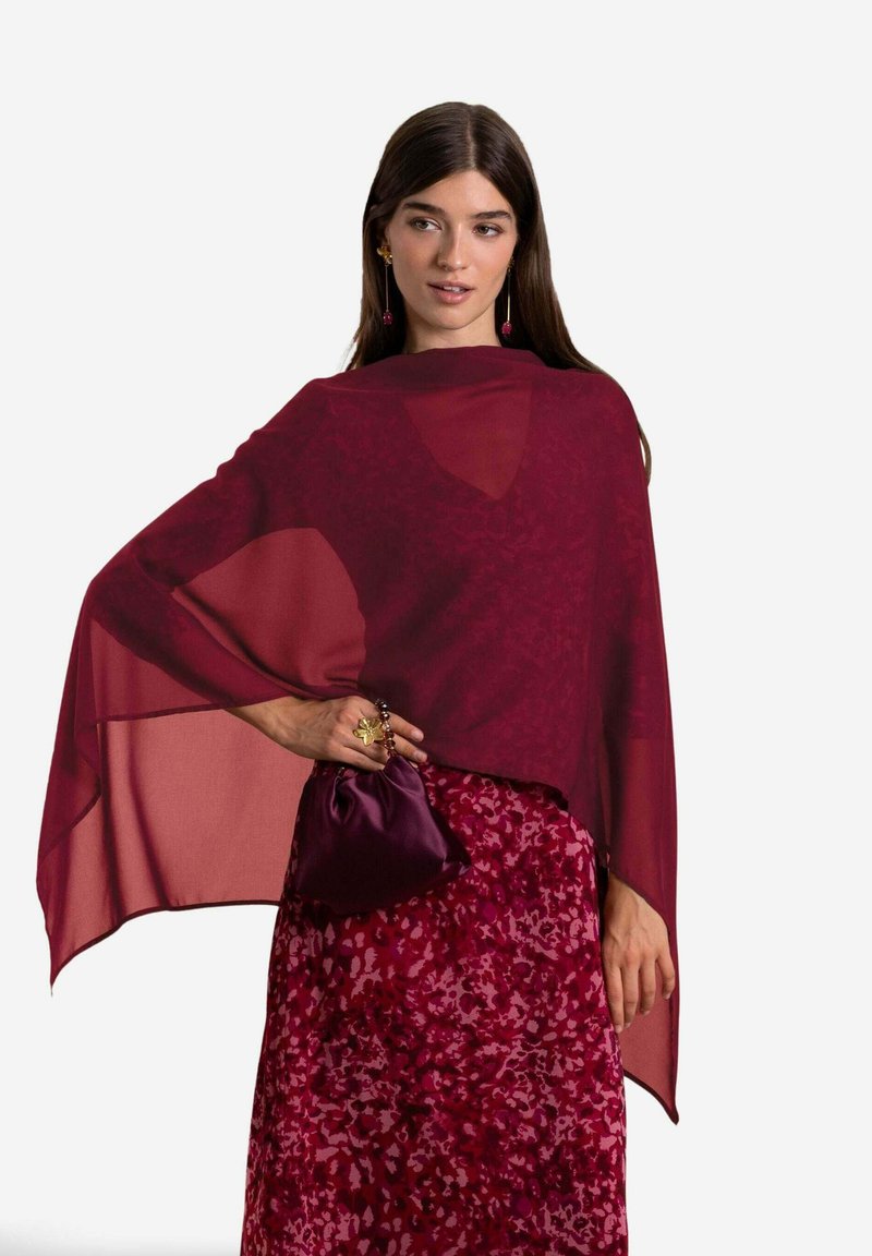 Chal de chiffon burdeos cae sobre una falda burdeos estampada. Los accesorios incluyen un bolso de mano a juego y un anillo llamativo.