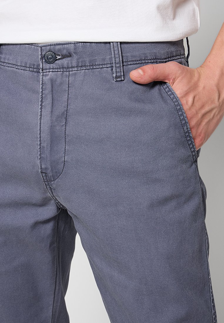 Pantalones de algodón gris con corte recto, bolsillos frontales y cierre de botón, que muestran una textura suave y sutiles detalles de costura.