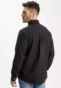 Czarna koszula z długim rękawem, z klasycznym kołnierzykiem, zapinanymi mankietami i gładką fakturą, noszona z niebieskimi dżinsami, widok z tyłu.