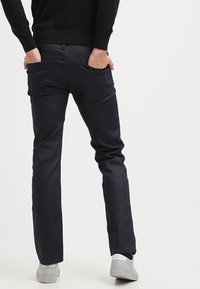 Mörkblå jeans med slim fit, som har två bakfickor och subtila sömnadsdetaljer. Åt kombinerade med ljusgrå sneakers för kontrast.