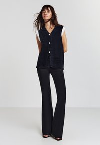 Gilet di tessuto blu con bottoni, con maniche a coste bianche. Abbinato a pantaloni neri a palazzo e scarpe open-toe.