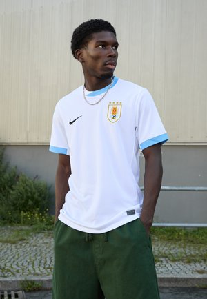 White soccer jersey with light blue accents; features team crest with stars, Nike logo, and mesh texture. Paired with green shorts.
