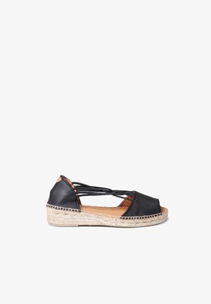 Espadrille en cuir noir avec bout ouvert, brides entrecroisées et semelle en jute tressé. Design plat, doublure intérieure contrastante tan et accent décoratif.