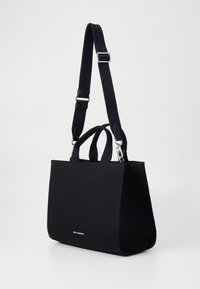 Bolso de lona negro con dos asas cortas y una correa larga ajustable. Presenta un gancho de presión plateado y un logo sutil en el frente.